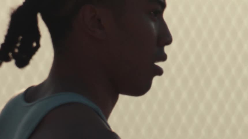A close-up slow-motion shot reveals a focused young man holding a basketball on a court during golden hour