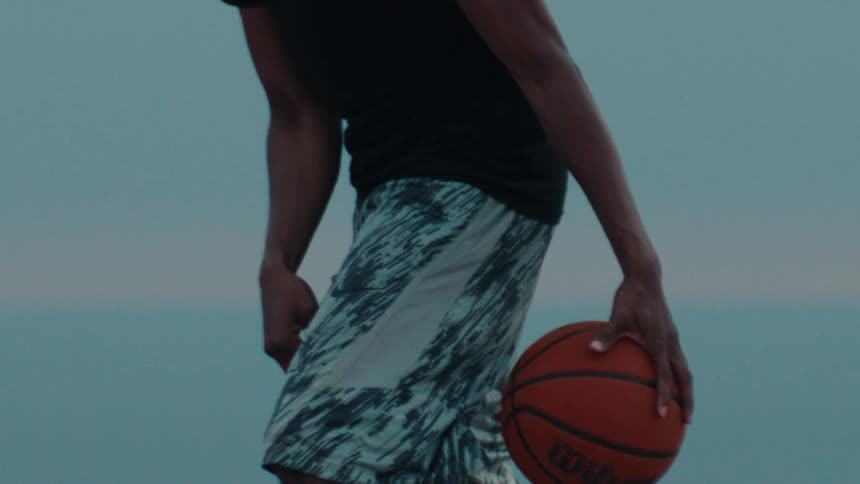 A basketball player dribbles a basketball in a cinematic slow-motion close-up