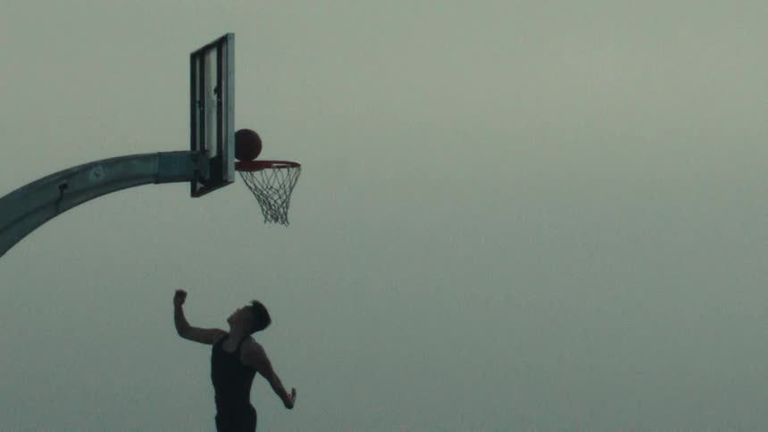 A basketball player makes a perfect jump shot in dramatic super slow motion against an overcast sky