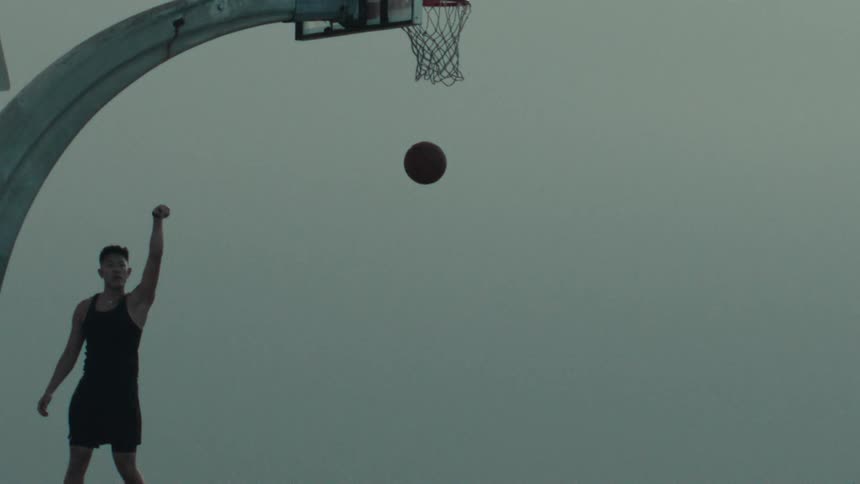 An athletic man holds his shooting form as a basketball swishes through the net in dramatic slow motion