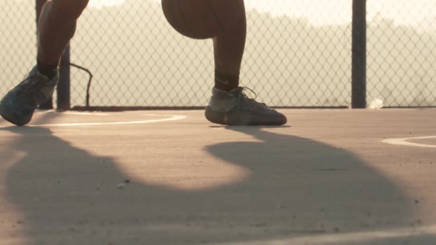 Close-up slow motion shot of a basketball player's feet dribbling and jumping on an outdoor court at sunset