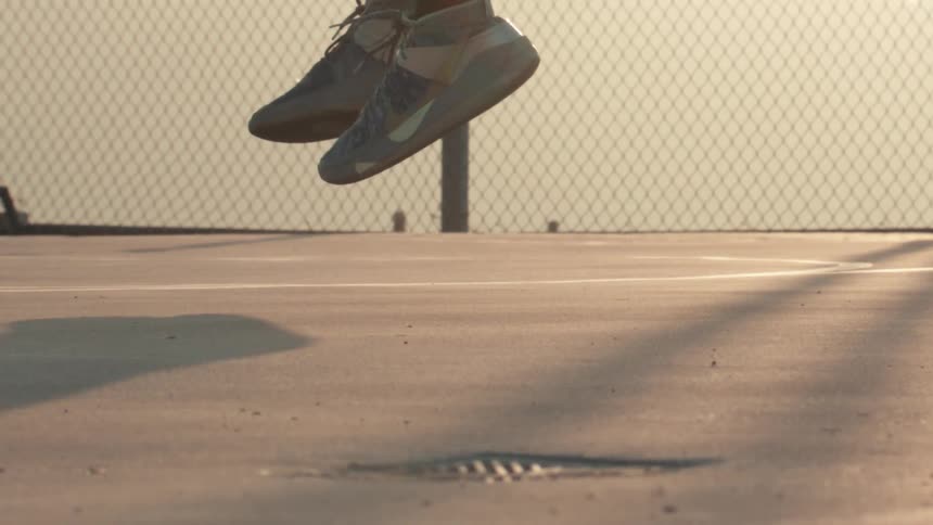 An athlete's feet lift off the ground in super slow motion while jumping on an outdoor court at golden hour