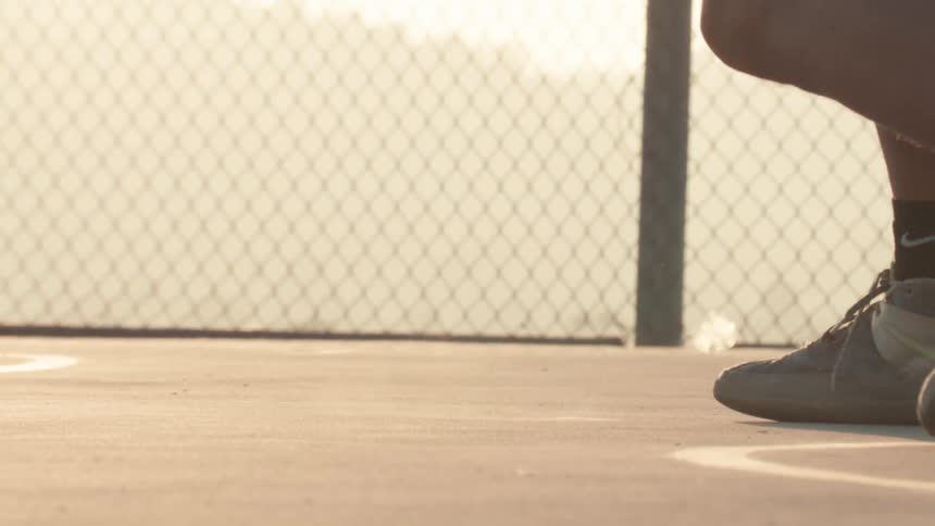 A basketball player dribbles the ball in slow motion on a concrete court during a beautiful sunset