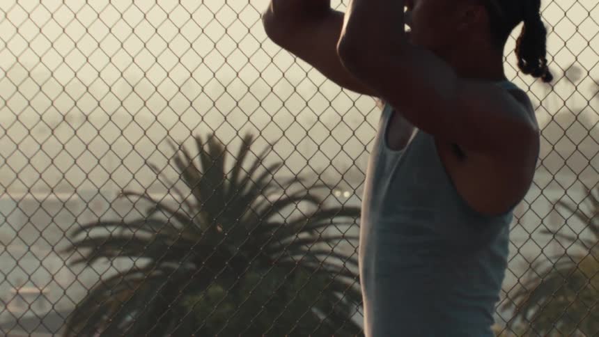 An athletic young man in slow motion prepares to take a basketball shot on a caged urban court at sunset