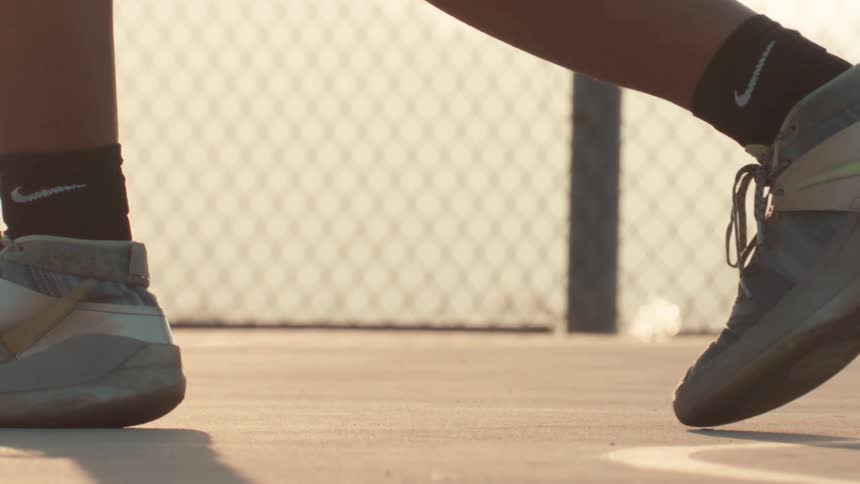 A basketball player's sneakers grip the court as they dribble a ball in slow motion during a warm sunset