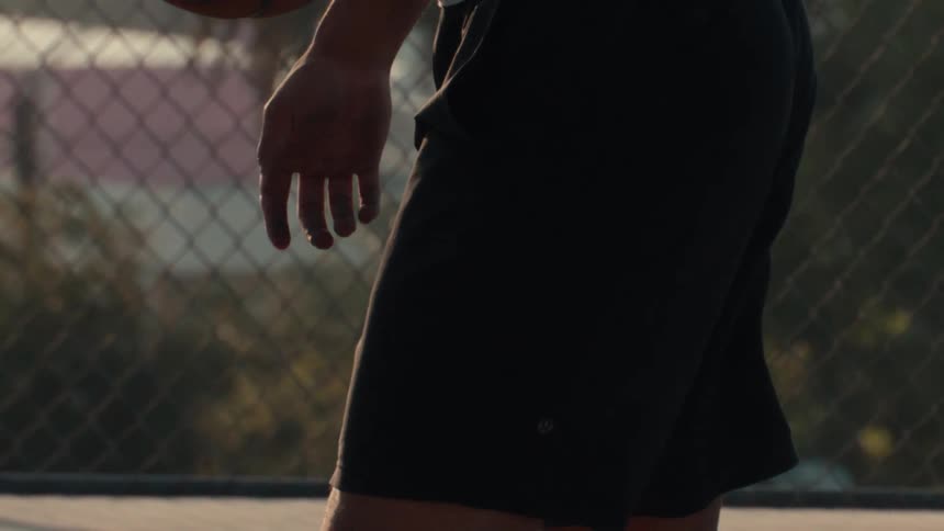 A basketball player takes a breath while holding the ball on an outdoor court in cinematic slow motion