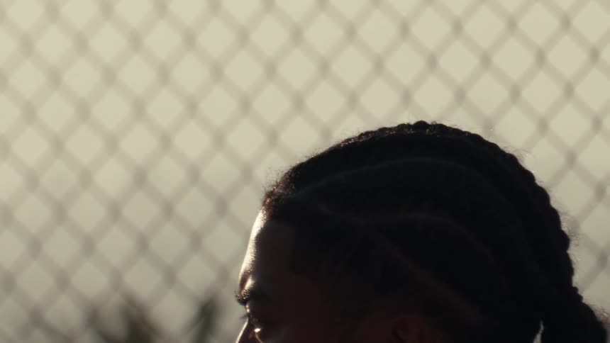 A dramatic slow-motion close-up reveals a focused young Black athlete with braided hair catching his breath