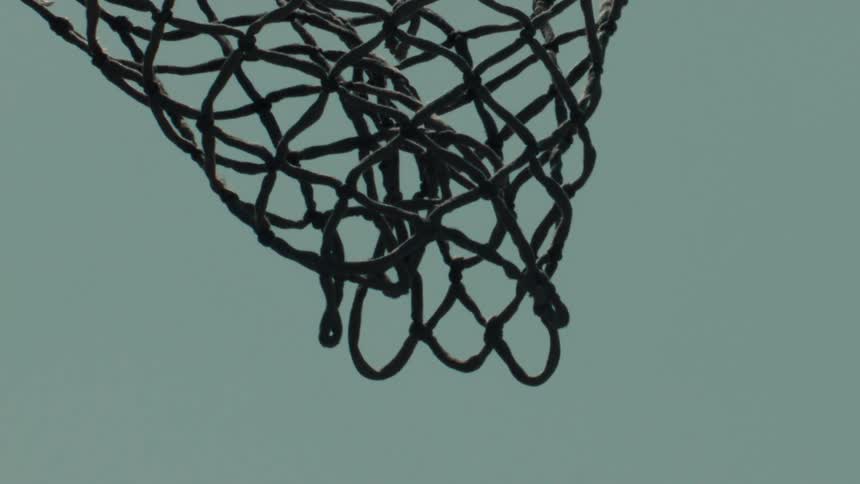 A basketball goes through a chain net in slow motion against a clear sky