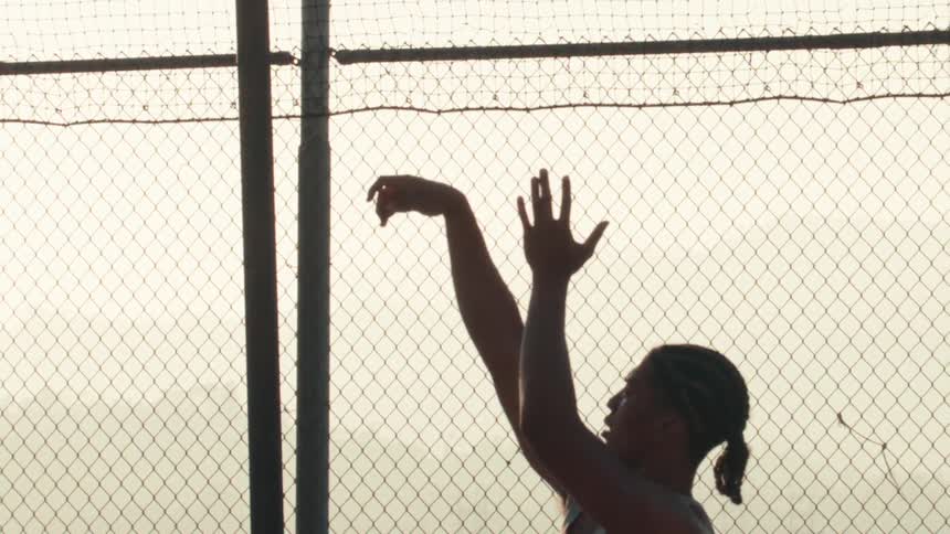 A silhouetted man performs slow-motion pull-ups on an urban court against a hazy sunrise