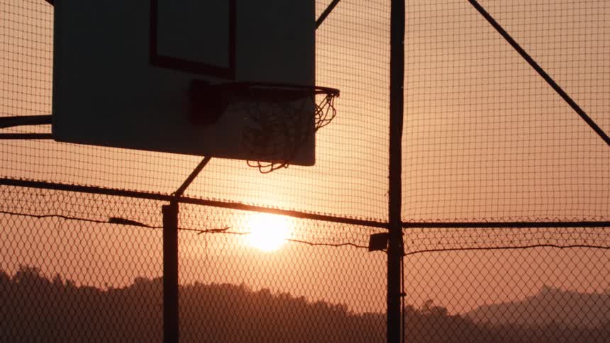 A basketball swishes through the net in slow motion with the golden sun setting in the background