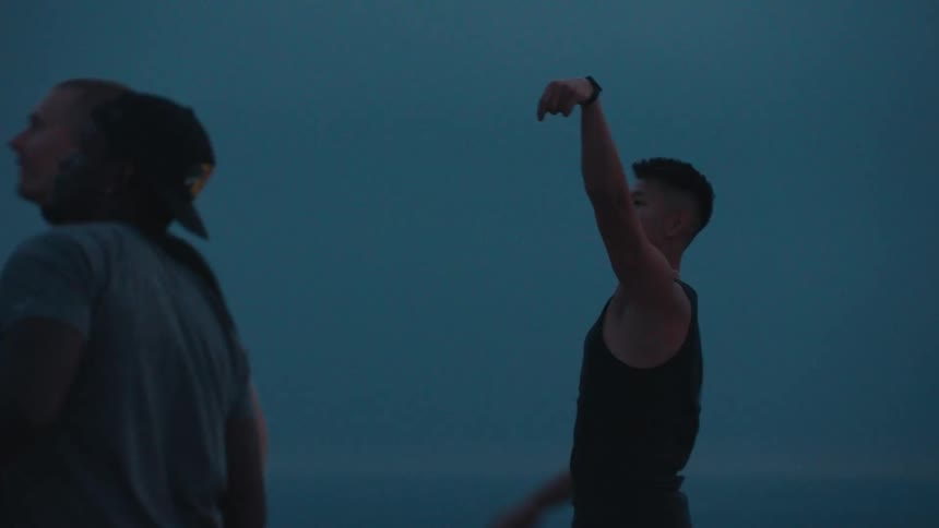 An athletic man takes a shot playing basketball with friends on an outdoor court at dusk in slow motion