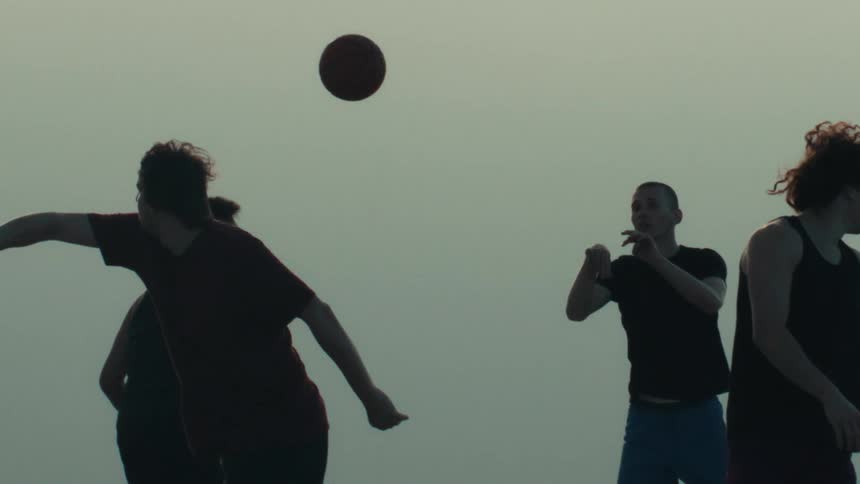 Silhouettes of young men play a game of street basketball as one player makes a throw in super slow motion