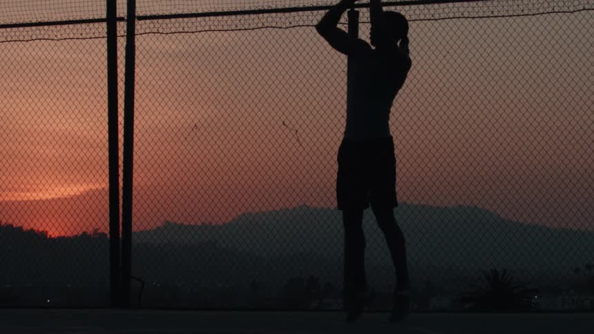 A silhouetted basketball player takes a jump shot in super slow motion on an outdoor court at sunset