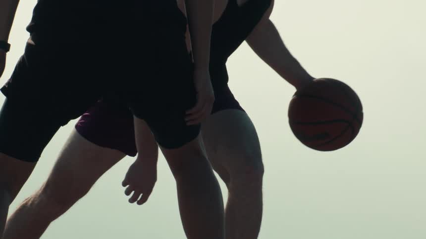 Two basketball players face off in an intense slow-motion game against a bright, hazy sky