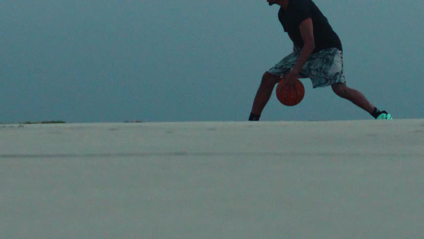 In super slow motion, a man dribbles a basketball across a vast, empty white landscape