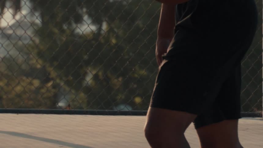 Cinematic slow motion shot of a basketball player preparing to play on an outdoor court during golden hour