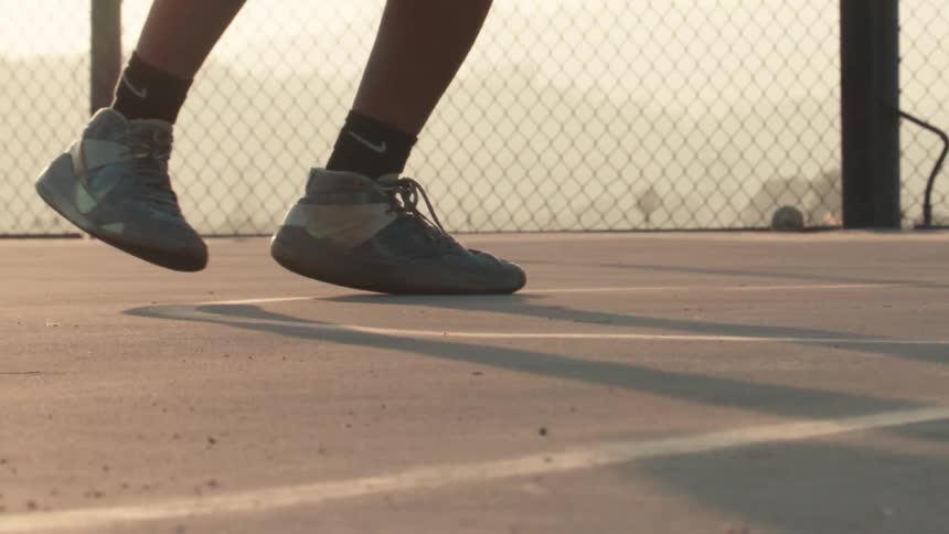 In a cinematic slow-motion close-up, a basketball player's sneakers grip the court while dribbling before taking flight at golden hour