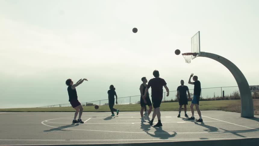 Silhouetted friends play basketball in super slow motion on an outdoor court, with multiple balls soaring towards the hoop