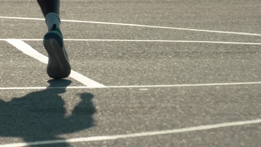 Close-up on the feet and shadows of a group of athletes walking in slow motion on a paved court