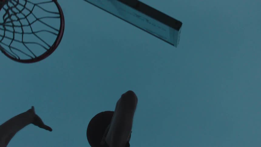A determined basketball player makes a perfect shot into the hoop in slow motion, captured from a low angle against a moody evening sky