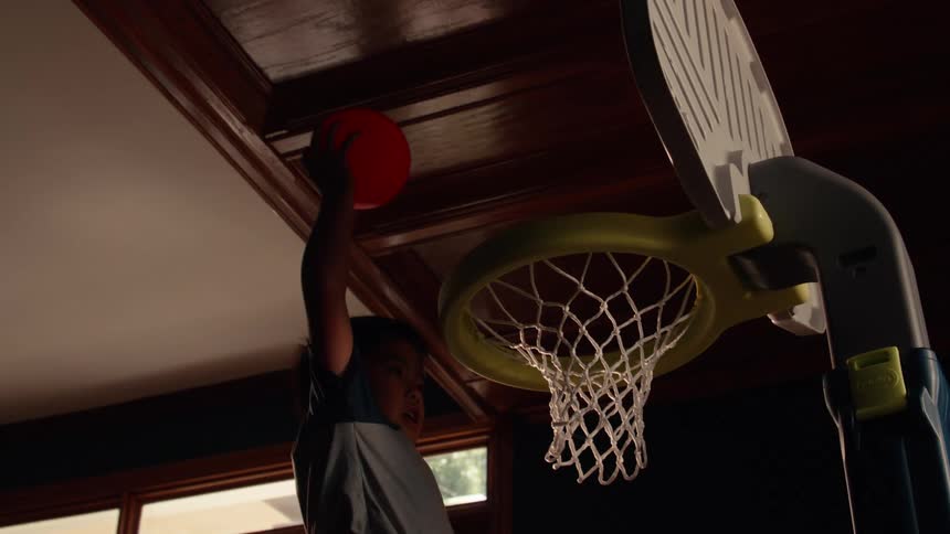 A young boy dunks a red basketball into a toy hoop in slow motion