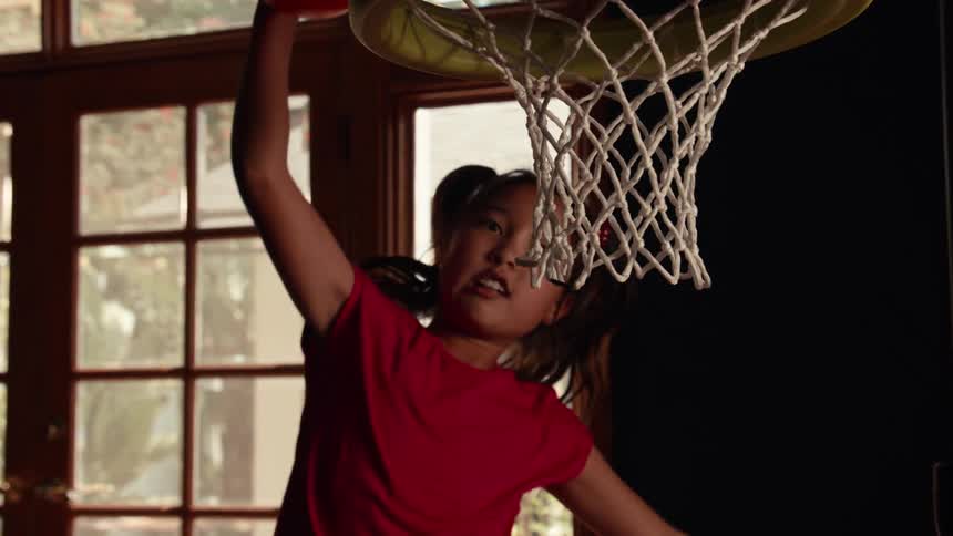A young girl with pigtails makes an impressive slam dunk into a toy basketball hoop in super slow motion