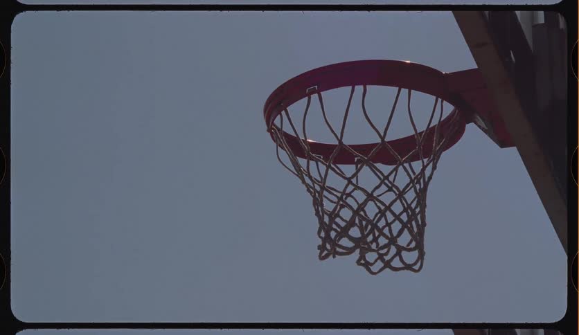 A vintage, low-angle shot of an outdoor basketball hoop against a clear summer sky