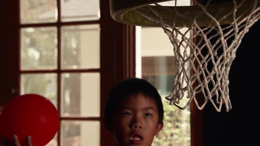A determined young boy slam dunks a red ball into a toy basketball hoop in dramatic slow motion