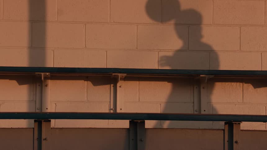 A shadow of a person slowly dribbles a basketball against a brick wall during the warm glow of sunset