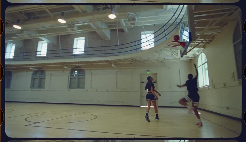 A man drives to the basket and scores a layup against a woman defender during a one-on-one basketball game on a classic indoor court in slow motion