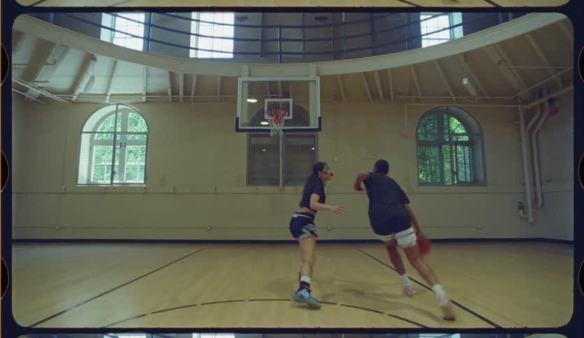 A male basketball player dribbles past a female defender and scores a layup in slow motion on an indoor court