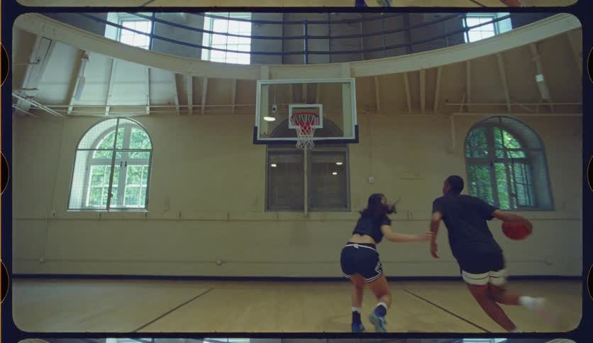 Slow motion shot of a man making a basket while playing one-on-one with a woman in a vintage-style gym