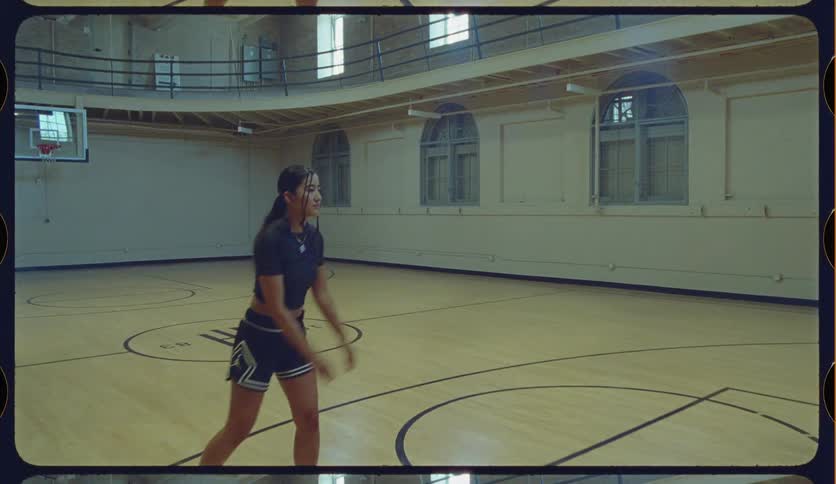 A female athlete catches a basketball and takes a jump shot in slow motion on a vintage indoor court