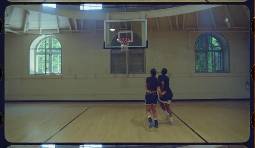 A man skillfully makes a layup against a woman during a one-on-one basketball game on a vintage indoor court in slow motion