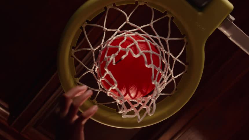 From a low angle perspective, a small red basketball is dunked through a toy hoop in slow motion