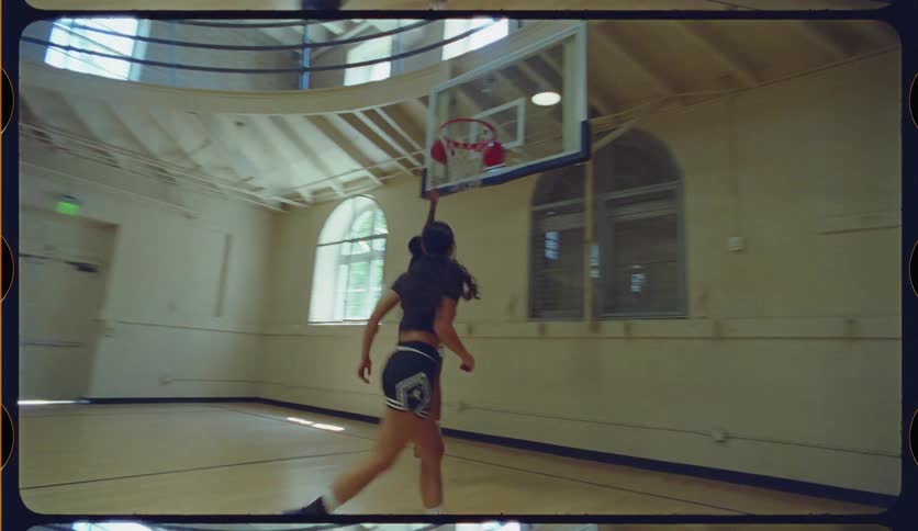 A man dribbles past a female defender and scores a layup during a basketball game in a sunlit gymnasium