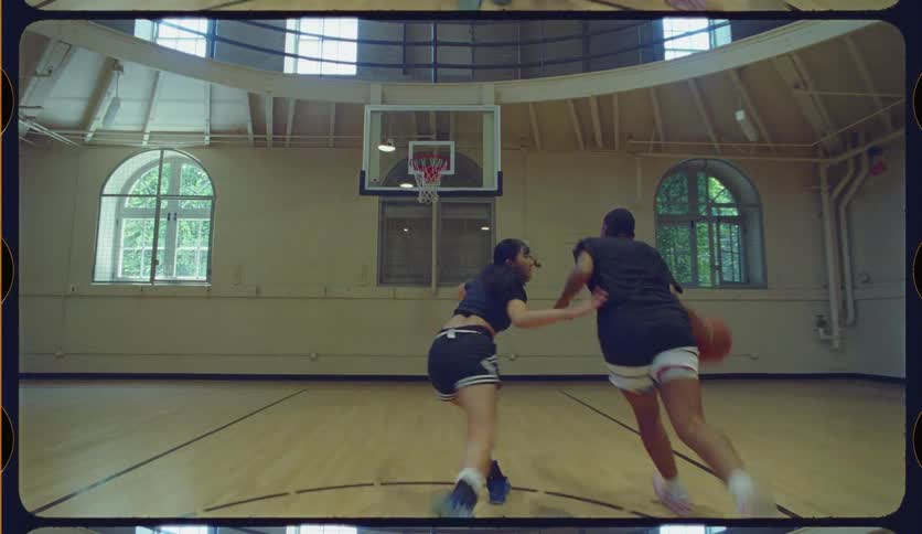 In slow motion, a man dribbles past a woman and scores a layup in a vintage basketball court