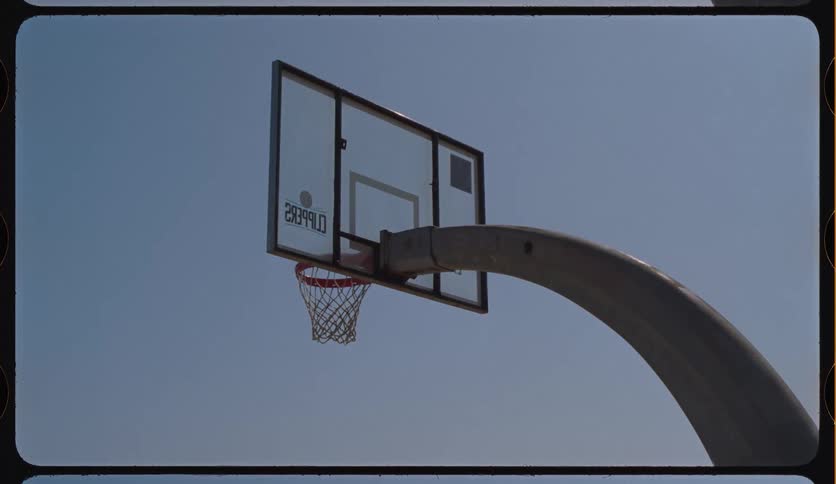 An outdoor basketball hoop with a transparent backboard and chain net stands still against a clear blue sky