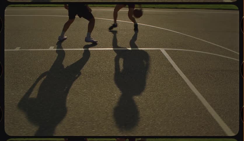High-angle shot captures the shadows of two basketball players in a one-on-one game on an outdoor court at sunset