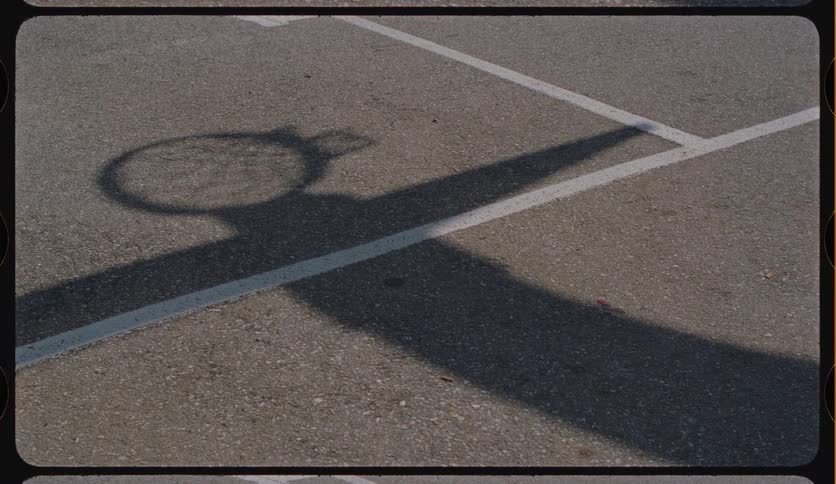 A vintage-style film scan captures the shadow of a basketball hoop on an empty outdoor court