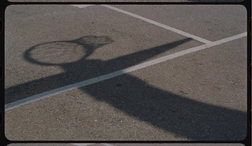 A basketball's shadow scores a perfect shot through the shadow of a hoop on an asphalt court