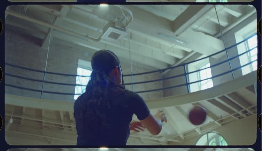 Slow motion low angle shot of a woman with long hair shooting a basketball on an indoor court with vintage film effects