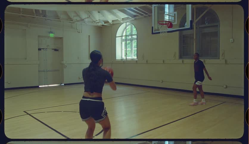 Two female athletes practice shooting and passing in slow motion on an indoor basketball court