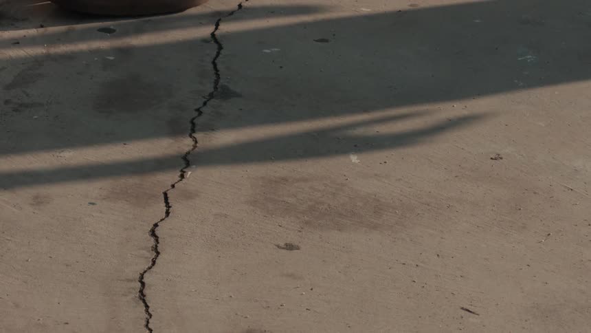 A moving shadow is cast across a long crack in a concrete floor
