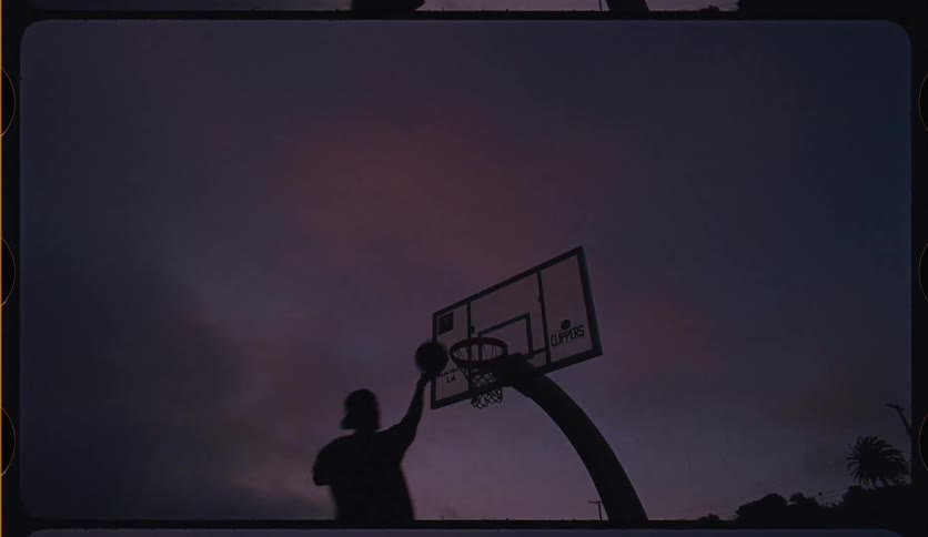 A person successfully shoots a basketball into a hoop in silhouette against a dramatic purple sky at dusk in a slow-motion, vintage film-style shot