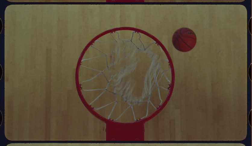 A basketball swishes through the net in slow motion from a birds-eye perspective with a retro film look