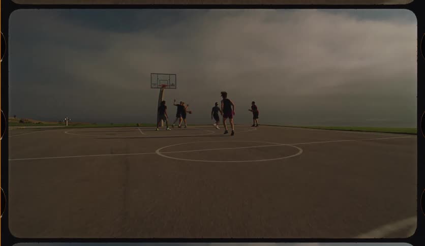 Friends play a game of pickup basketball on a seaside court under a dramatic sky in a nostalgic, slow-motion shot