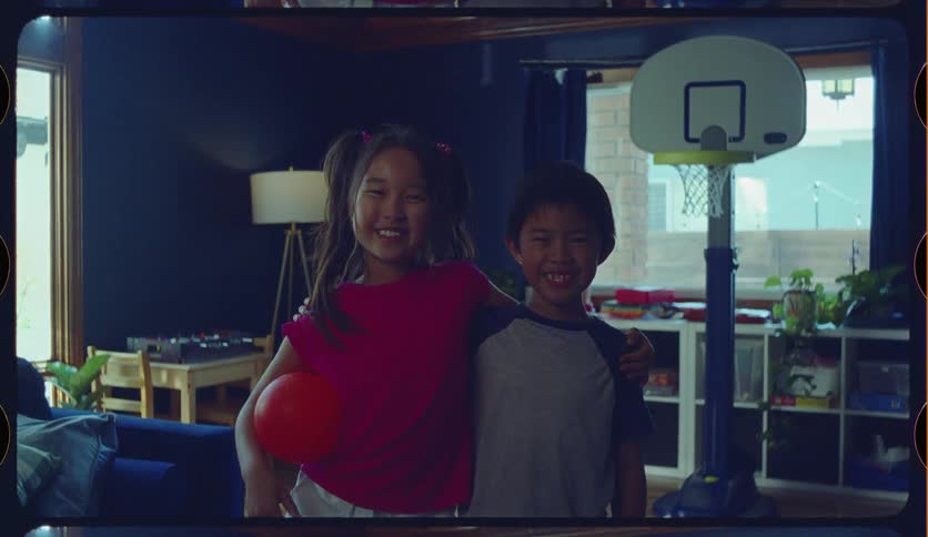 A vintage-style home movie clip shows a happy Asian brother and sister smiling for the camera in their playroom