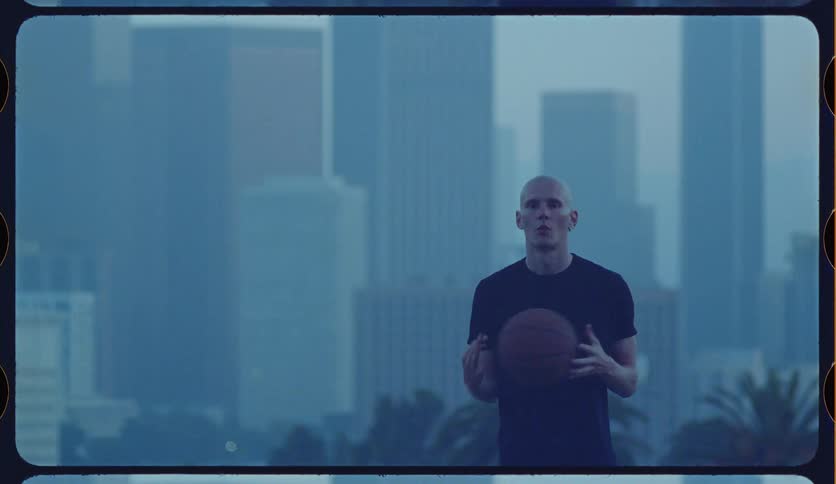A male basketball player explains techniques while holding a ball in front of a hazy city skyline