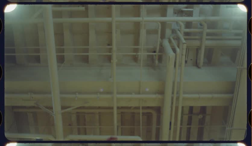 Low angle view of a person repeatedly shooting a basketball towards an industrial ceiling on a vintage film reel